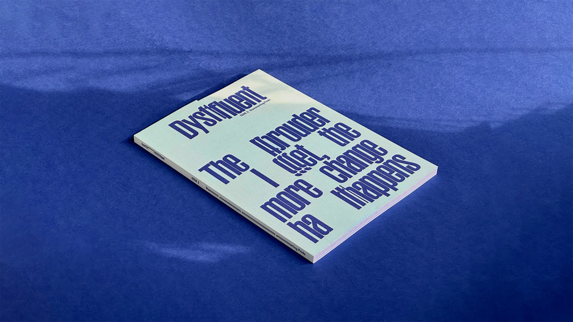 A magazine on a dark blue surface. Its front cover is light seagreen with dark blue typography.