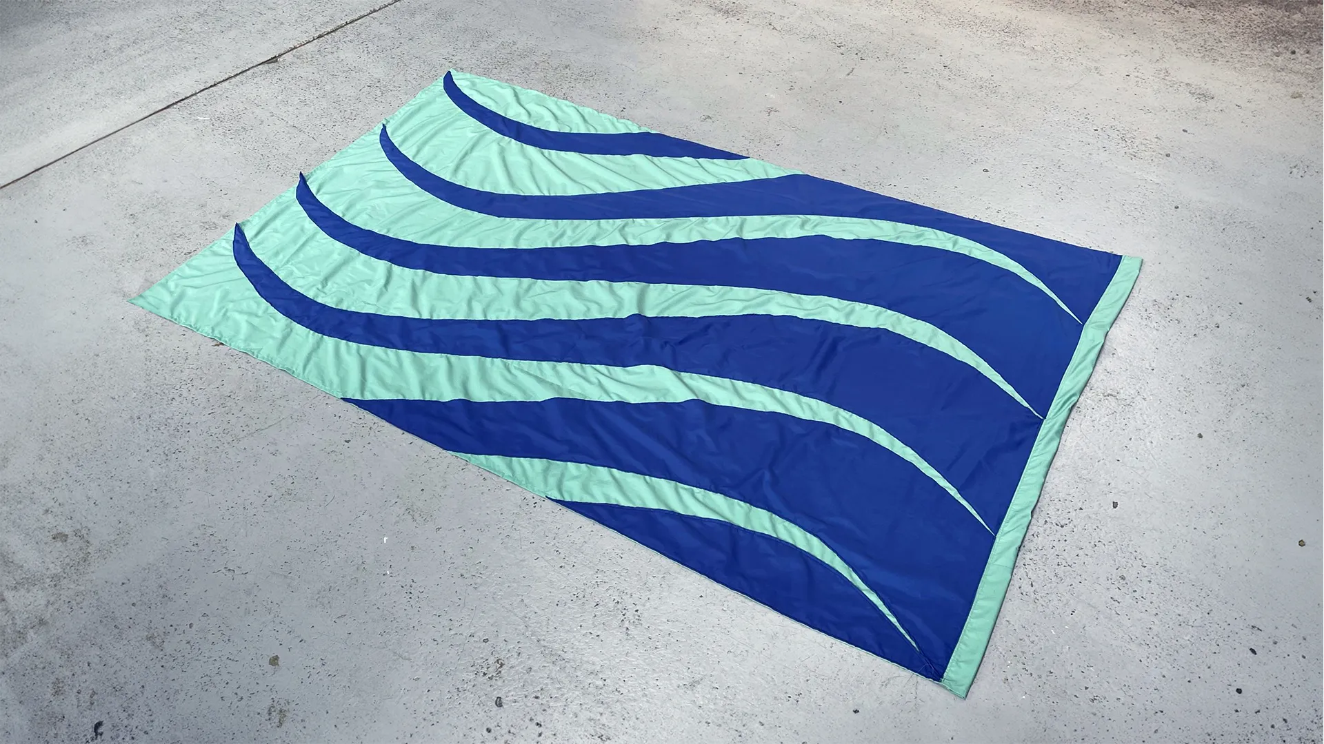 A flag on a concrete floor. The flag is seagreen and ultramarine blue waves.
