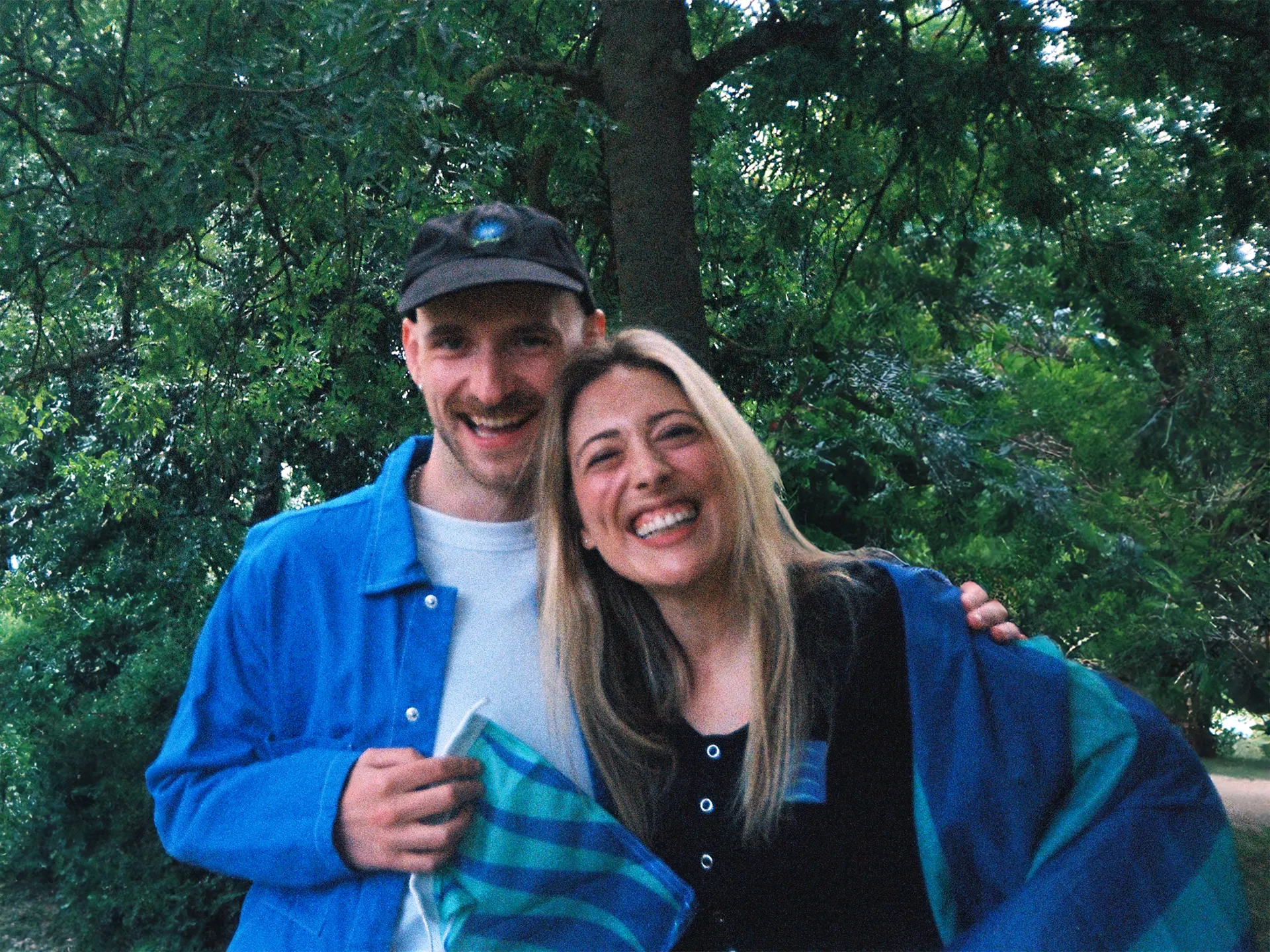 A smiling man and woman have their arms wrapped around each other. They are holding small flags of seagreen and ultramarine blue waves.