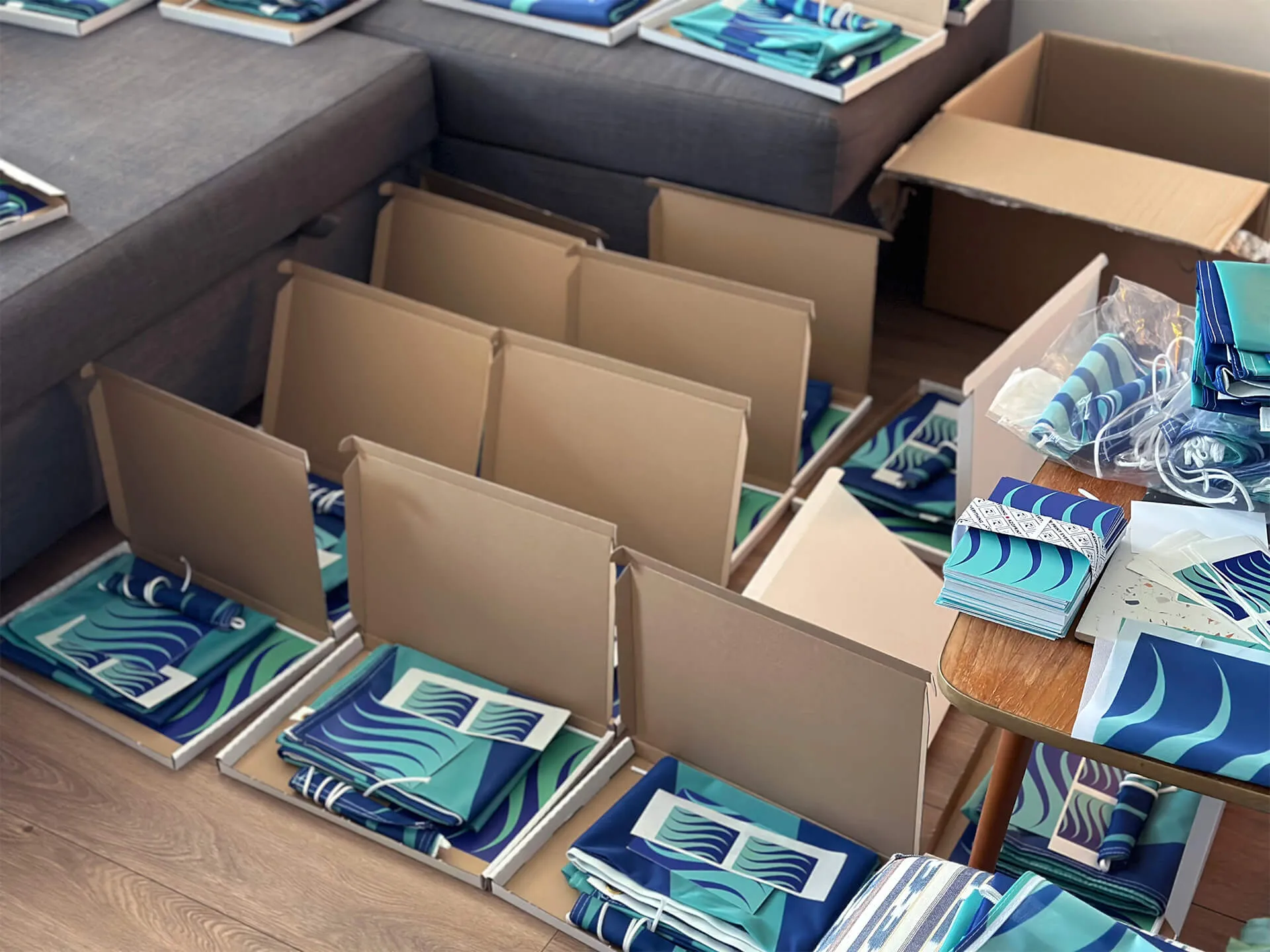 Numerous boxes are on the floor, containing stickers, postcards and flags. The flag design is seagreen and ultramarine blue waves. 