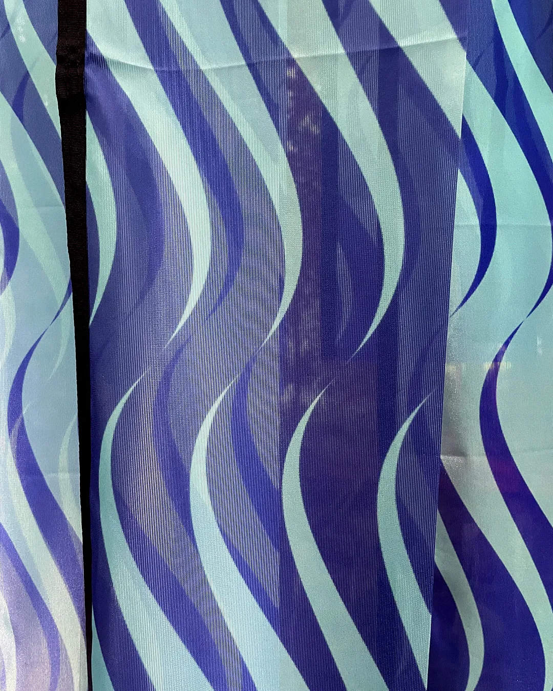 A close up of long strips of a repeat pattern on flag material. The repeat design is seagreen and ultramarine blue waves. 