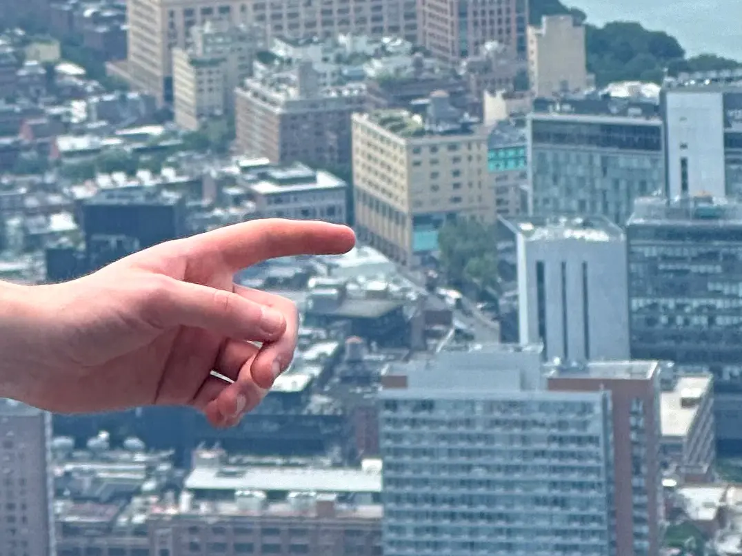 A hand points to the billboard way in the distance, as the photo was taken on a high building. 