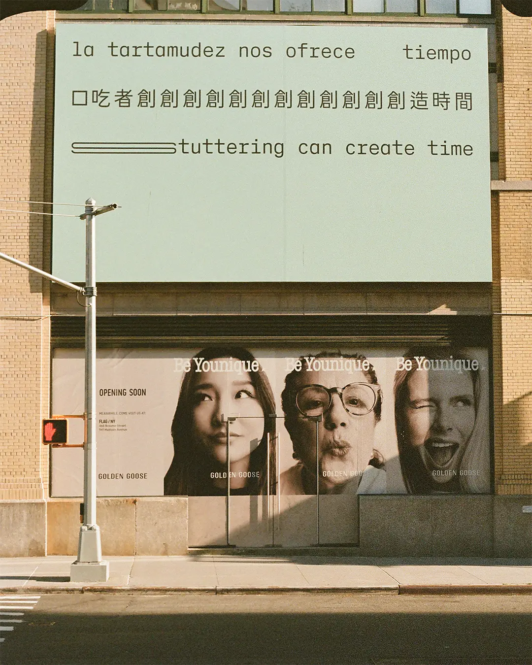 A film photograph of a billboard.  Three lines of black text appear on a light seafoam green background, in Spanish, Chinese and English, translating to: ‘Stuttering can create time.’ The text is in a sans serif typeface organised in three straight lines within the top half of the composition. The bottom half of the composition is empty. The text is stretched and repeated to represent stammering. 