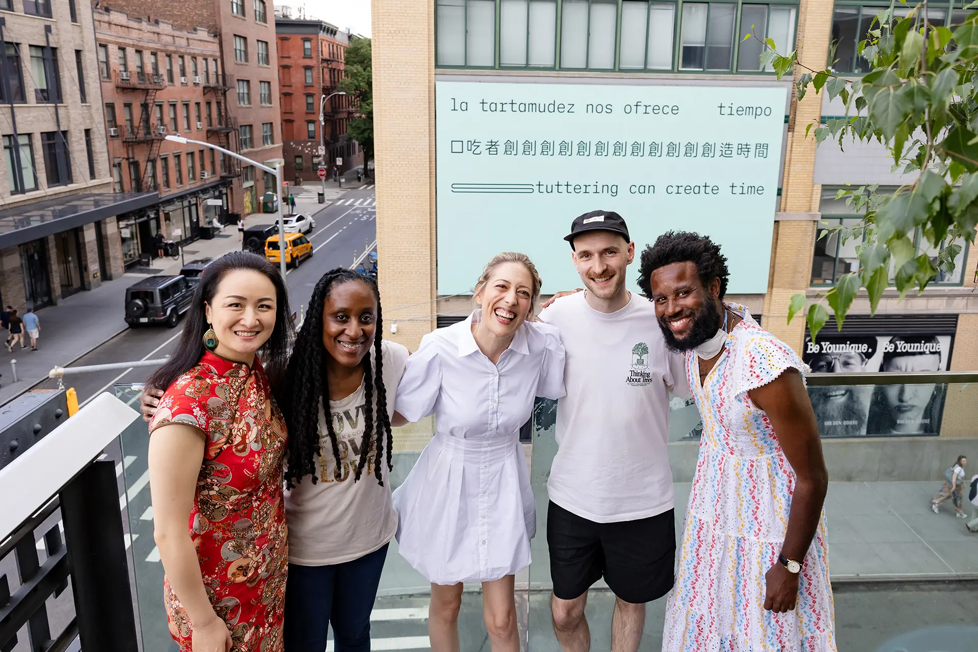 Five people stand together smiling, with the billboard seen behind them. 