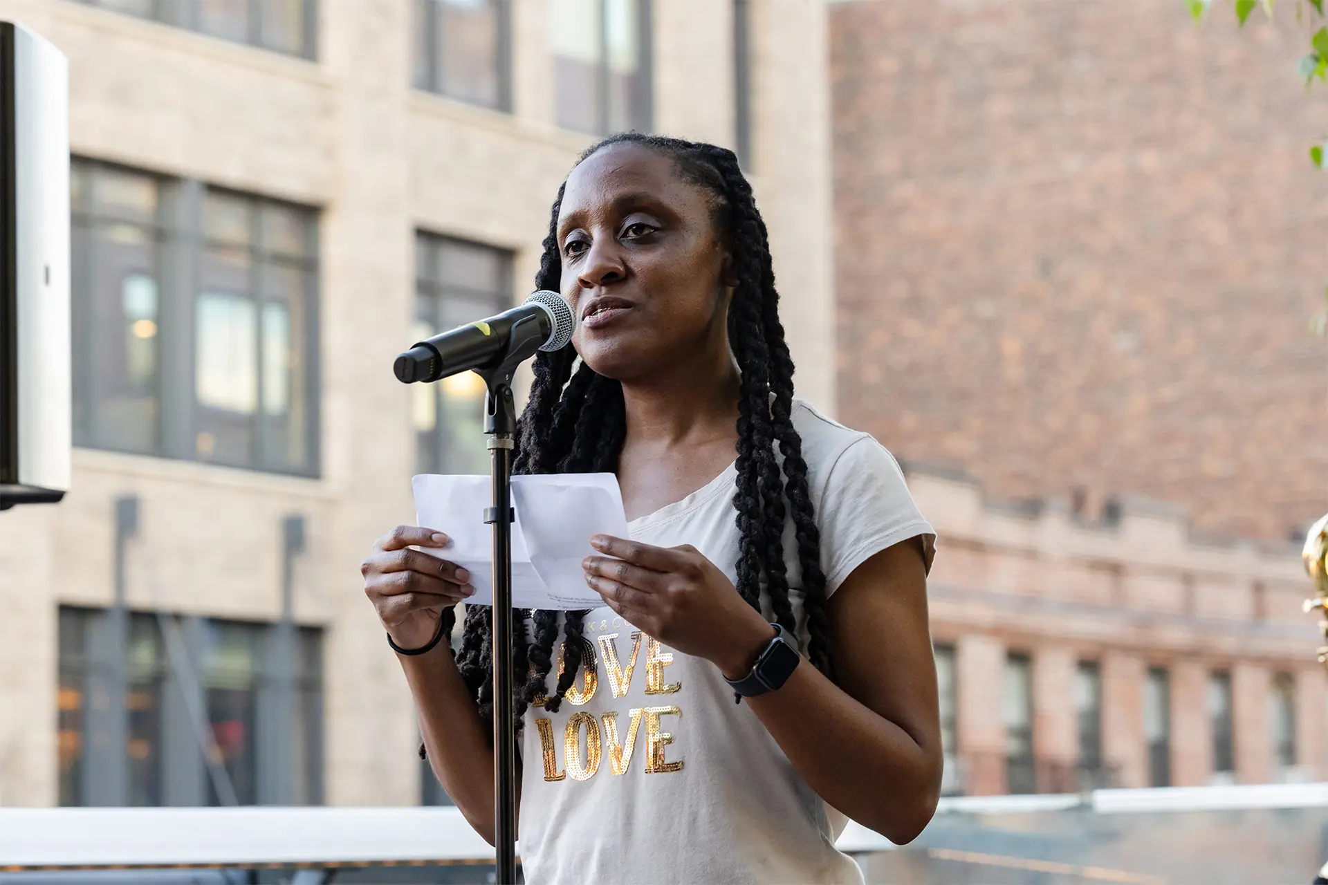 A woman speaks into a microphone, holding a piece of paper.