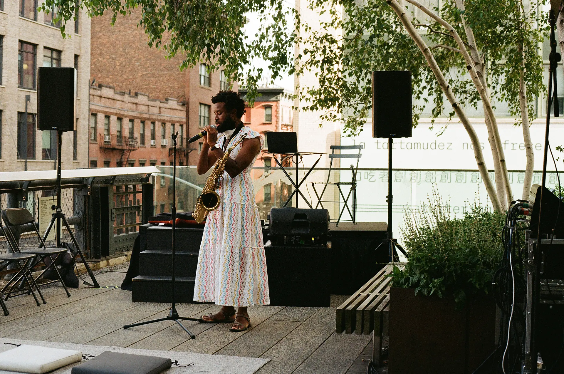 A brown-skinned person wearing a colourful dress sings into a microphone. 