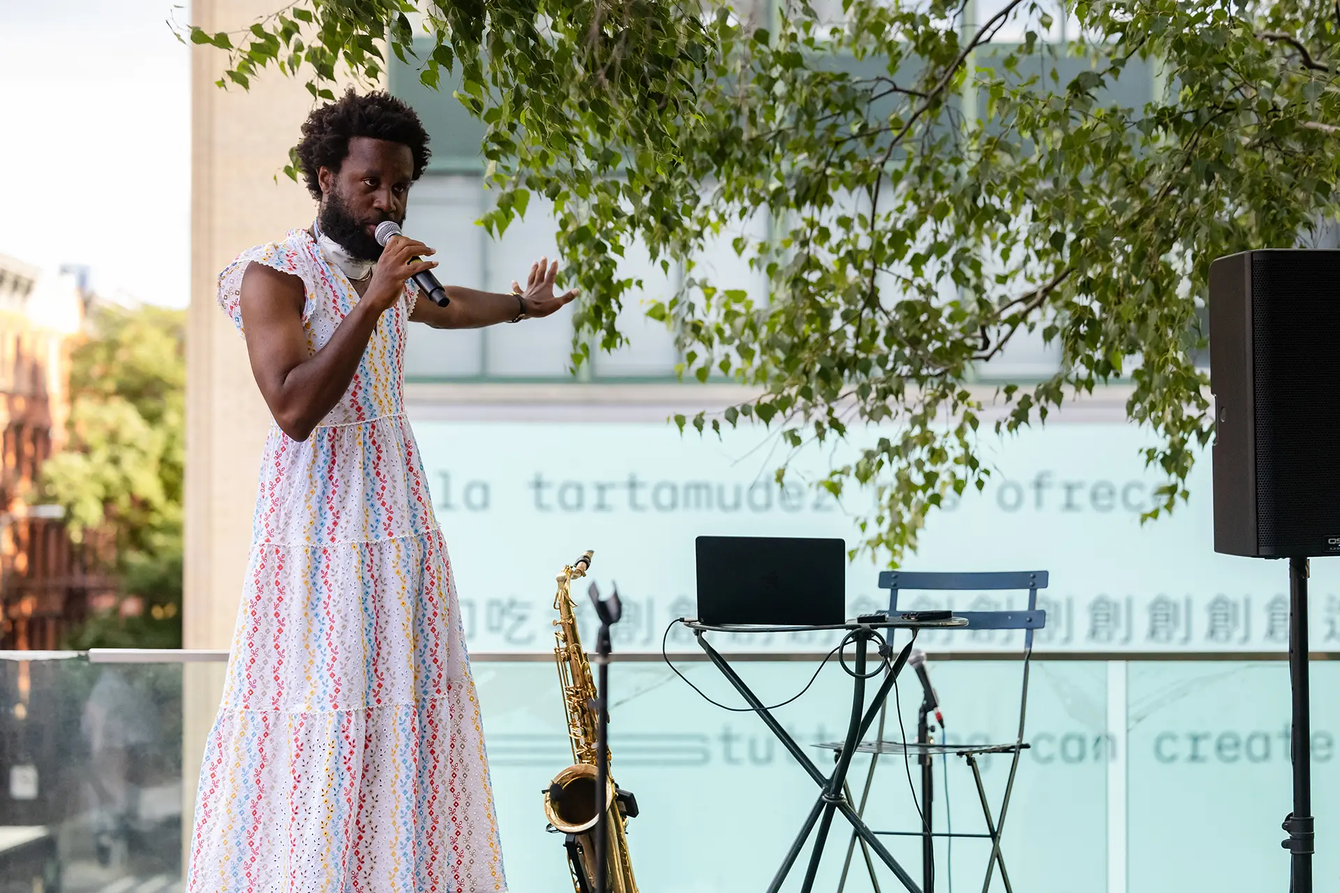 A brown-skinned person wearing a colourful dress sings into a microphone. 