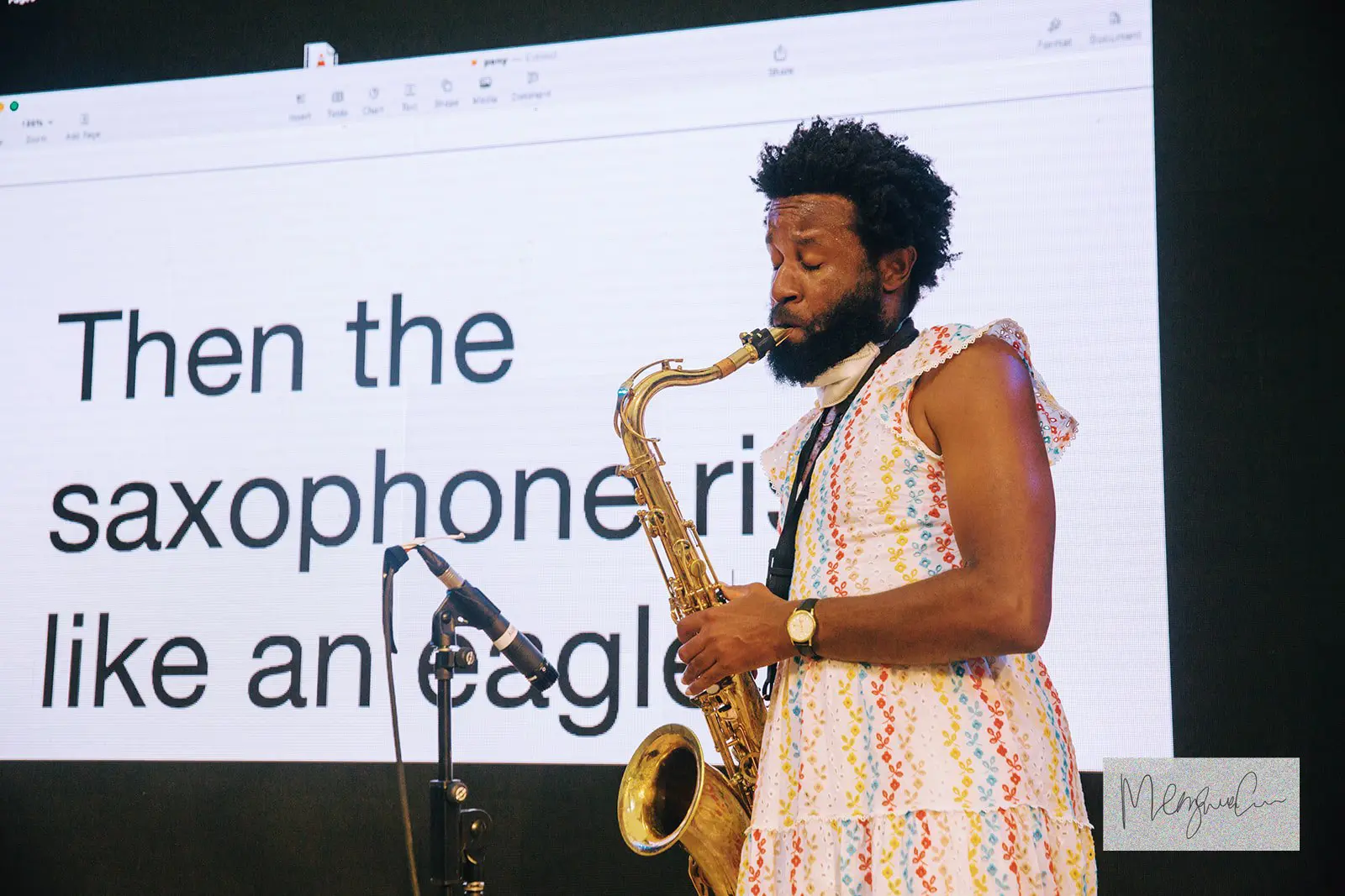 A brown-skinned person plays a saxophone. They are wearing a colourfully-embroidered dress and their eyes are closed.