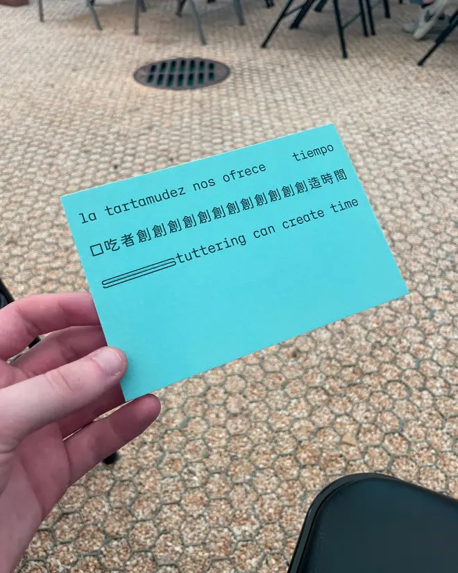 A hand holds a sea-green postcard with black text. 