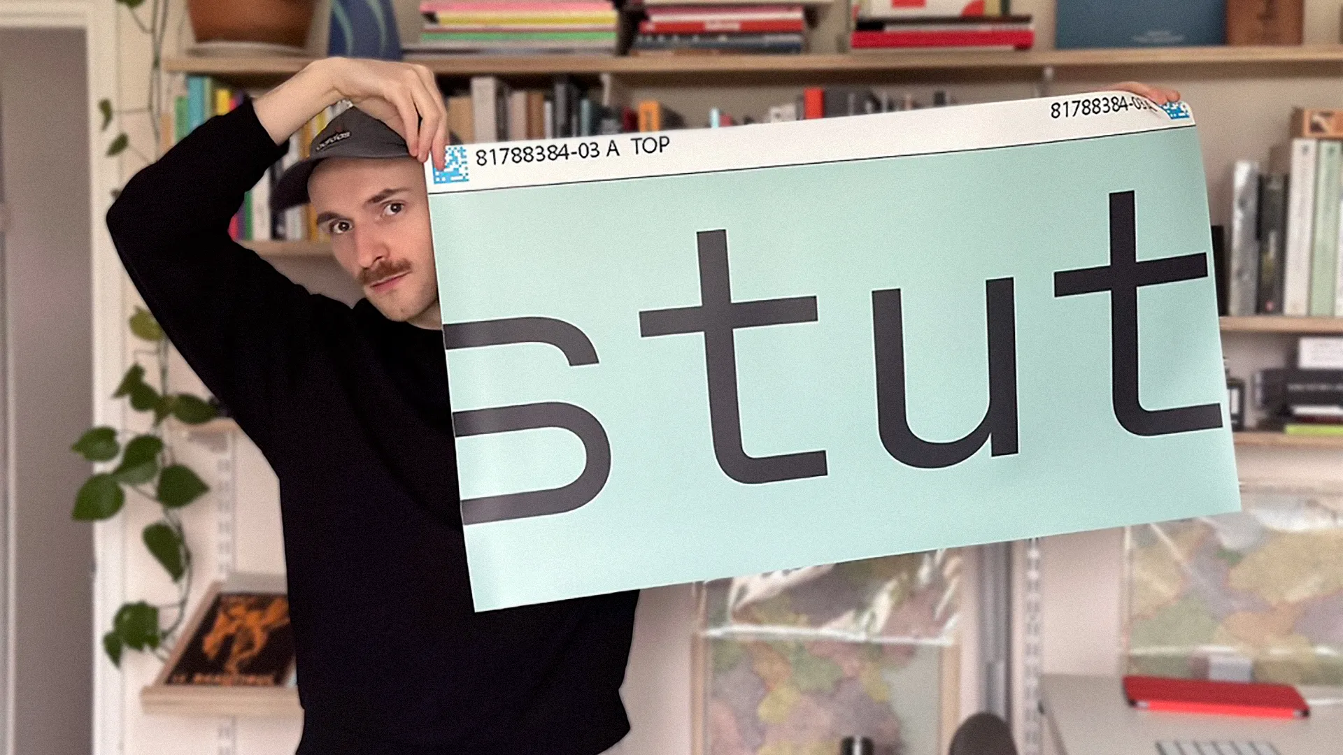 A young man holds up a large printed sheet with typography on it.